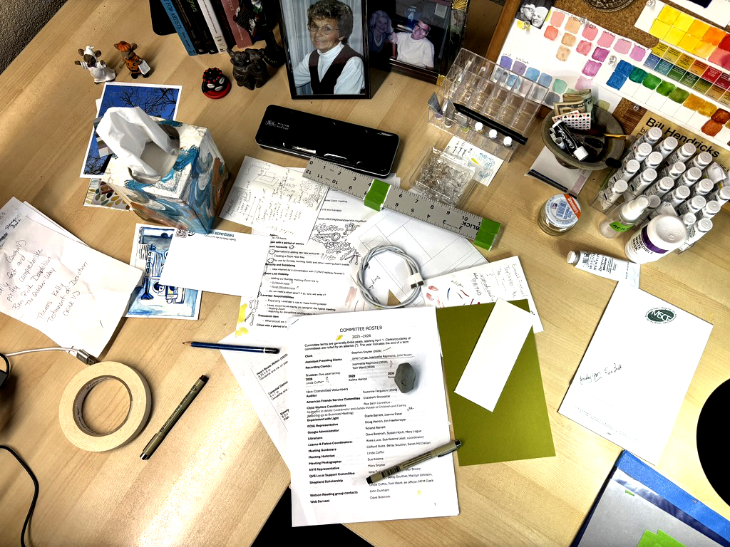 A softly lit artist’s desk scattered with sketches, notes, and bits of color — a quiet space of reflection where creative traces remain after the day’s work.